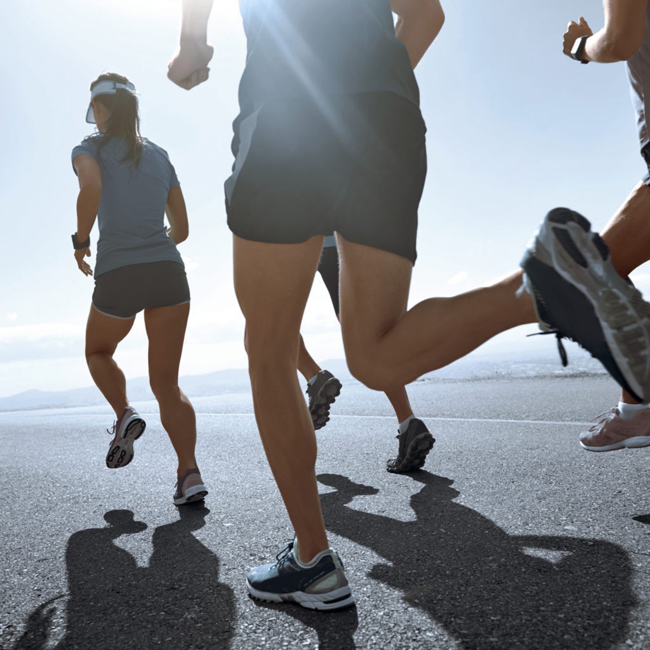 Nahaufnahme von Läufern in Shorts und T-Shirts, die bei hellem Sonnenlicht auf Asphalt rennen.